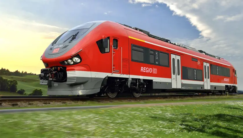 Roter Pesa-Zug der Deutschen Bahn fährt durch eine grüne Landschaft unter blauem Himmel.