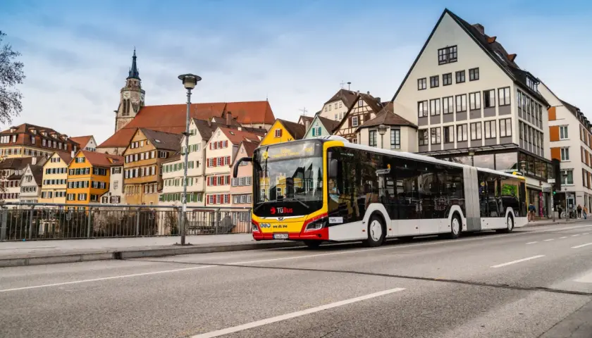 Ein langer ziehharmonika bus fährt an bunten Fachwerkhäusern vorbei.