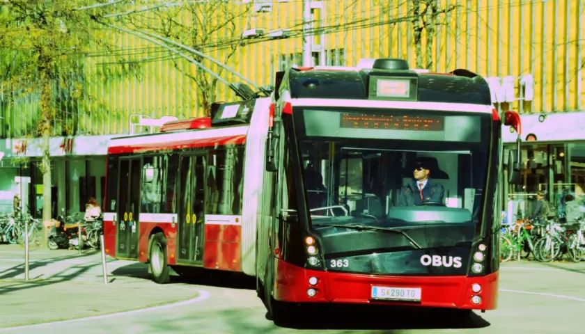 Ein roter Obus mit der Nummer 363 fährt auf der Straße. Der Fahrer trägt eine Sonnenbrille und eine Uniform.