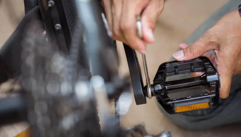 Hände reparieren ein Fahrrad. Ein Werkzeug wird angesetzt, um die Fahrrad Pedale knacken zu beheben.