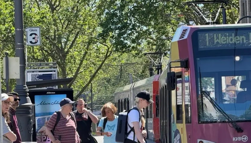 Menschen warten an Gleis 3 auf die Bahn. Die Anzeige zeigt "1 Weiden", was die einfache Fahrt Bedeutung für die Reisenden verdeutlicht.