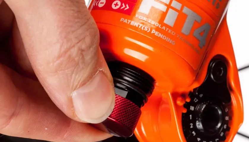 Hand dreht roten Knopf zur Federgabel einstellen. Rebound Adjust ist auf der orangefarbenen Gabel sichtbar.