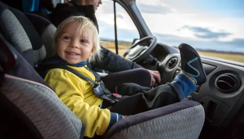 Glückliches Kind im Kindersitz im Bus. Die Füße des Kindes ragen über das Armaturenbrett.