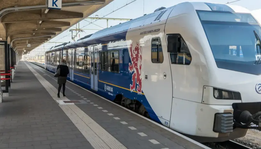 Eine Frau wartet auf dem Bahnsteig auf den Zug. Der blaue Arriva-Zug mit dem roten Löwenwappen ist ein Teil des Nahverkehrs in den Niederlanden.