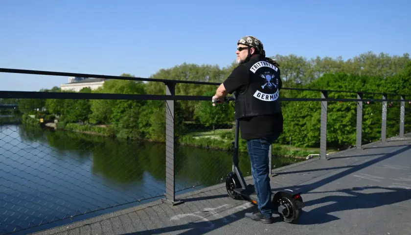 Mann mit Weste und Totenkopf-Bandana auf E-Scooter, genießt die Aussicht. Die Reichweite des E-Scooters ist für die Fahrt über die Brücke ausreichend.