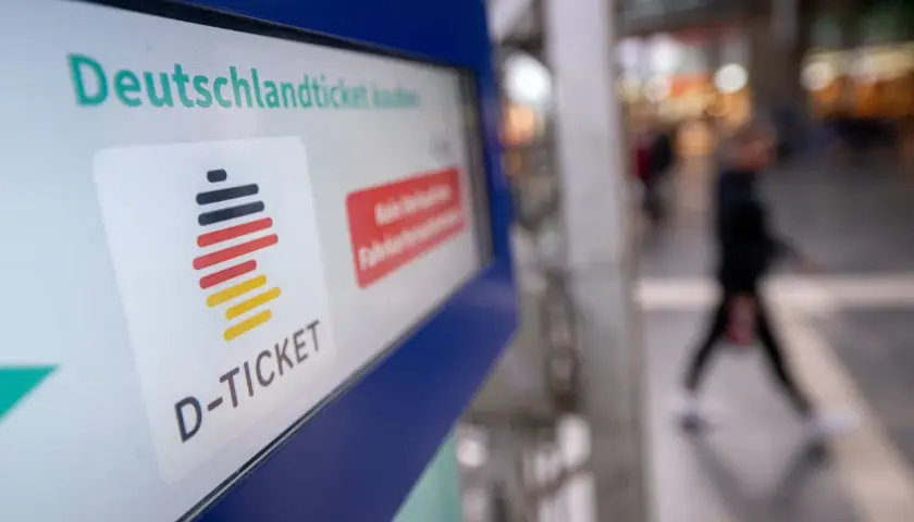 Das Deutschlandticket-Logo auf einem Bildschirm. Eine Person geht unscharf im Hintergrund vorbei. Vielleicht kann man das Deutschlandticket pausieren.