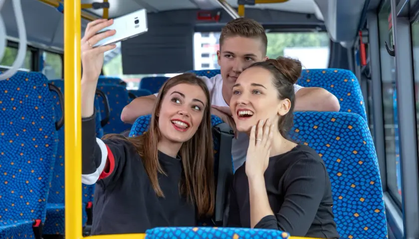 Drei junge Leute machen ein Selfie im Bus. Vielleicht sind sie auf dem Weg zu einem Konzert und hoffen, dass das Transdev Deutschlandticket keine Probleme macht.