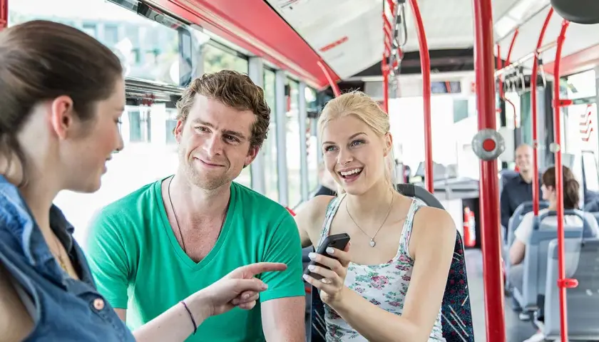 Drei Freunde unterhalten sich lachend im Bus. Sie fahren an Feiertagen NRW und genießen die gemeinsame Fahrt.