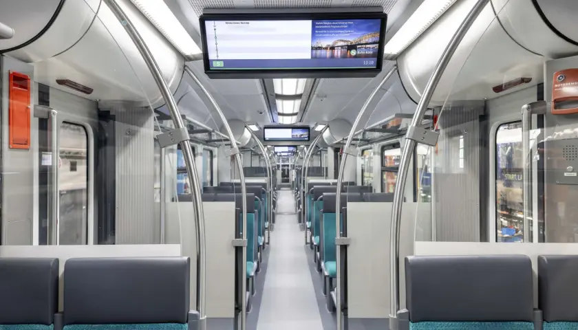 Innenraum eines modernen Zuges mit blauen Sitzen und einem Bildschirm, der die S-Bahn Köln zeigt. Die et 424 ist bereit für die nächste Fahrt.