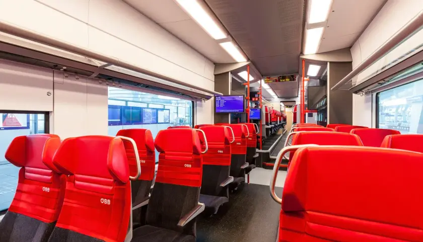Rote Sitze im modernen Desiro ML Zug der ÖBB. Die Sitze sind mit dem ÖBB-Logo versehen und laden zu einer angenehmen Reise ein.