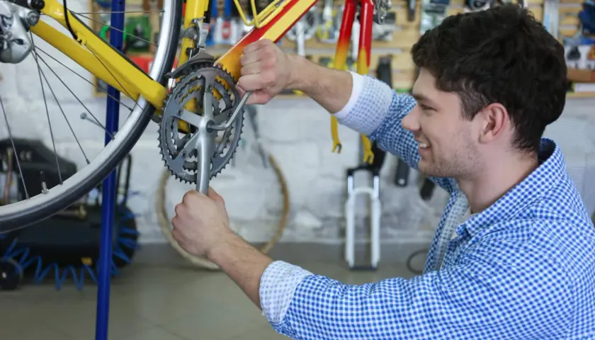 Ein Mann restauriert ein gelbes Fahrrad in einer Werkstatt. Er schraubt mit einem Werkzeug an der Kurbel.