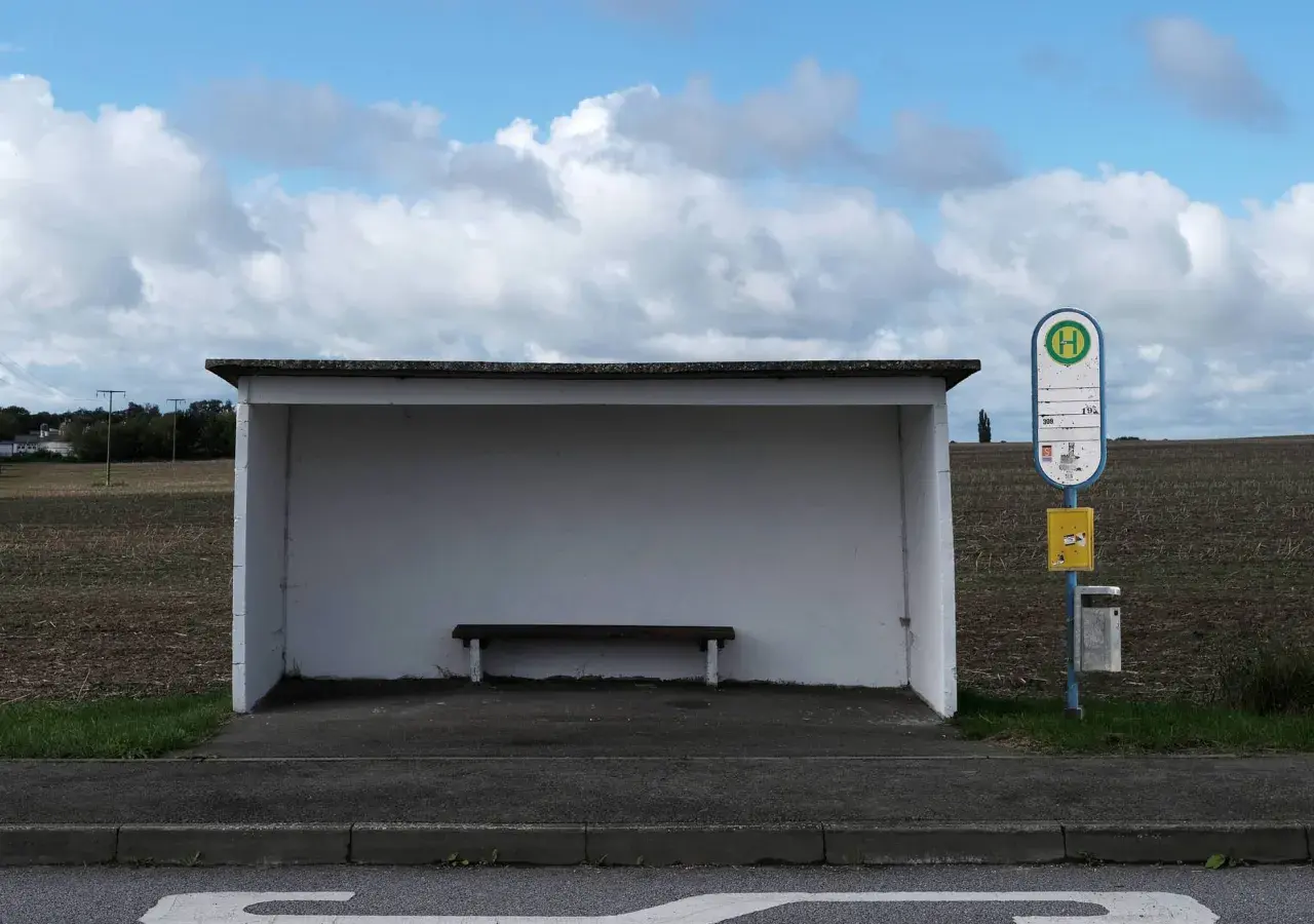 Ein Bushäuschen mit Bank und Haltestellenschild. Dieses Verkehrsmittel mit H-Symbol wartet auf Fahrgäste.