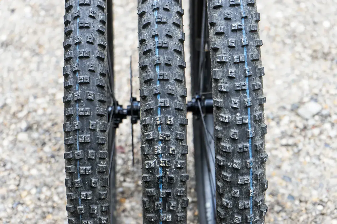 Drei breite Ballonreifen eines Mountainbikes mit grobem Profil und blauer Mittellinie. Bereit für jedes Gelände.
