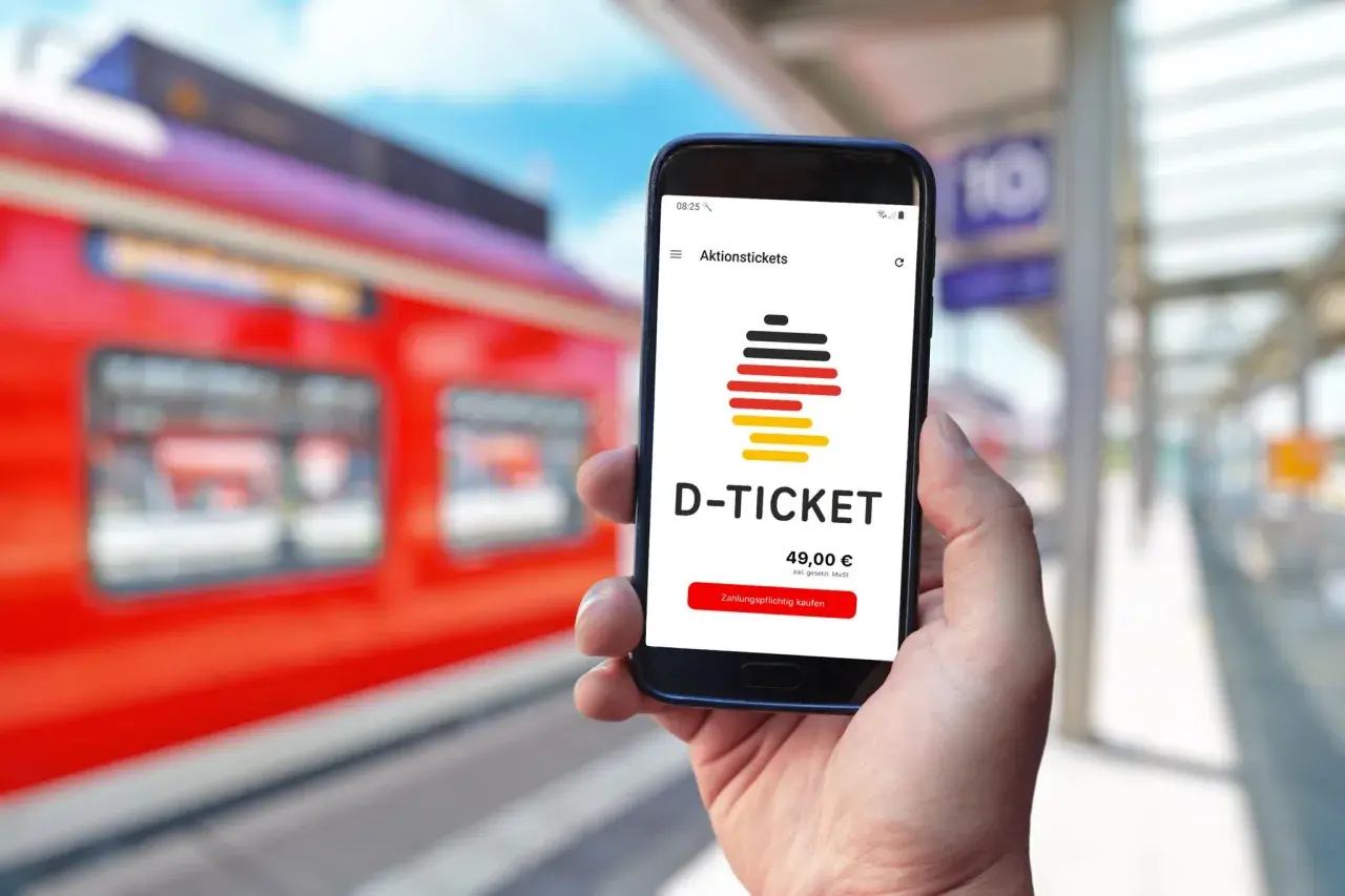 Hand hält Smartphone mit D-TICKET App, bereit für das quer-durchs-land-ticket wochenende. Zug am Bahnsteig.