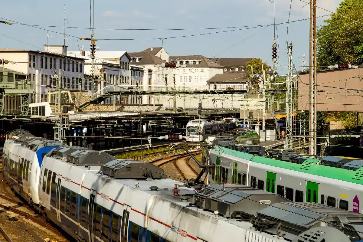 Zwei Züge stehen auf Gleisen vor Gebäuden. Ein Zug ist weiß mit roten Streifen, der andere grün. Perfekt für das db semesterticket nrw.