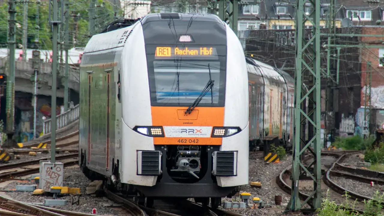 Ein moderner Zug der SPNV Linien NRW fährt auf Gleisen. Die Anzeige zeigt "RE1 Aachen Hbf".