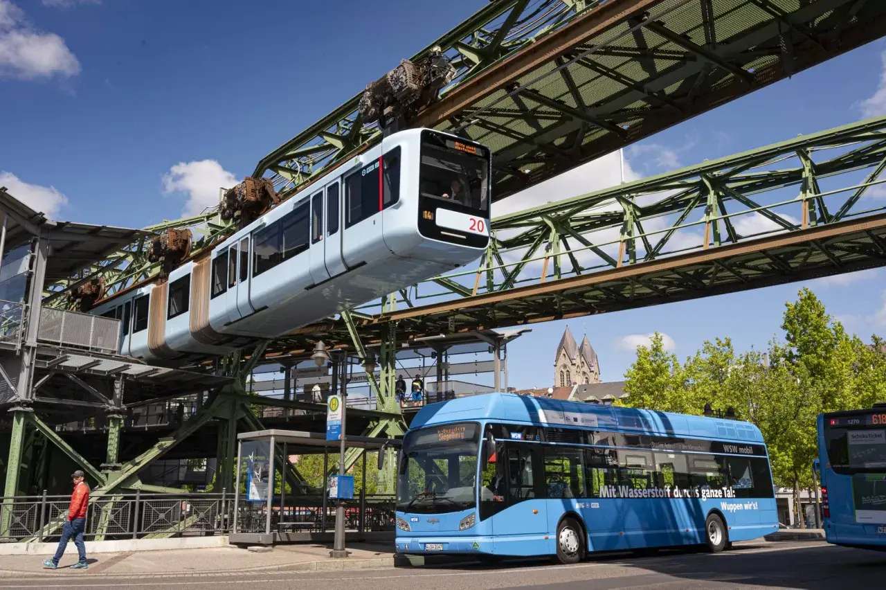 Die Schwebebahn Wuppertal fährt über einem blauen Bus. Mit dem Deutschlandticket ist das ganze Tal mobil.