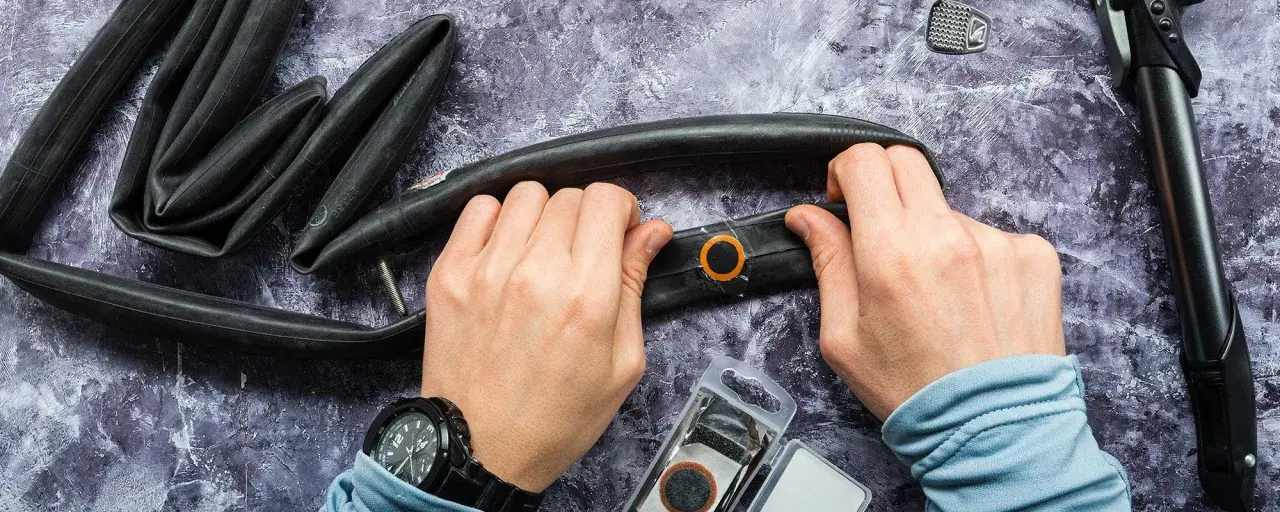 Hände reparieren einen Fahrradschlauch mit einem Flicken. Werkzeug und Flickzeug liegen bereit.