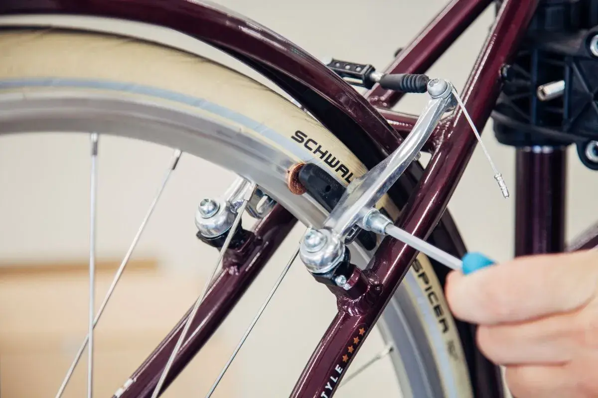 Hand wechselt Bremsbacken am Fahrrad mit Schraubendreher. Nahaufnahme des Bremsmechanismus am Rad.