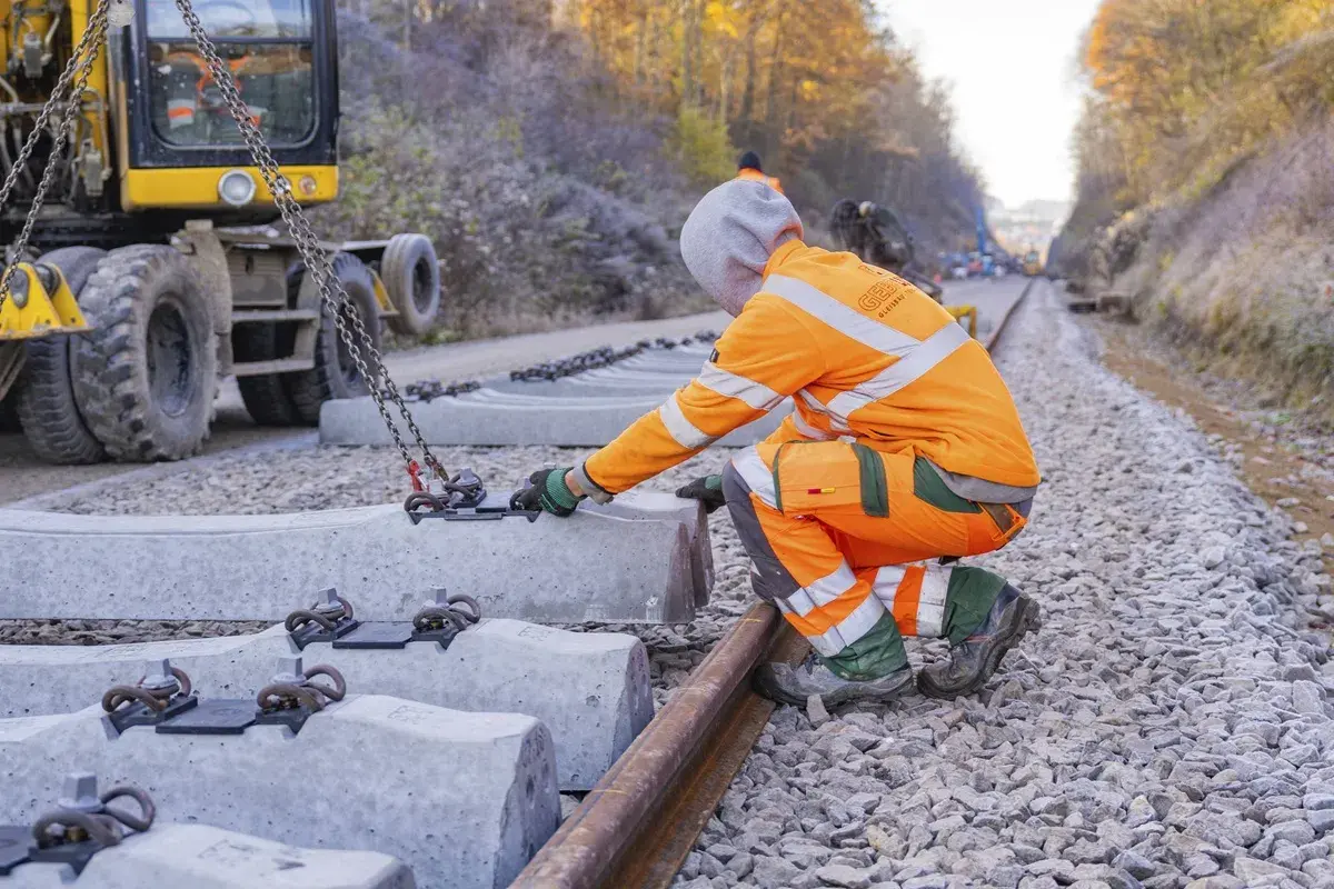 Arbeiter bei Bauarbeiten der Deutschen Bahn in NRW legen neue Betonschwellen. Ein Bagger hebt die schweren Teile an.