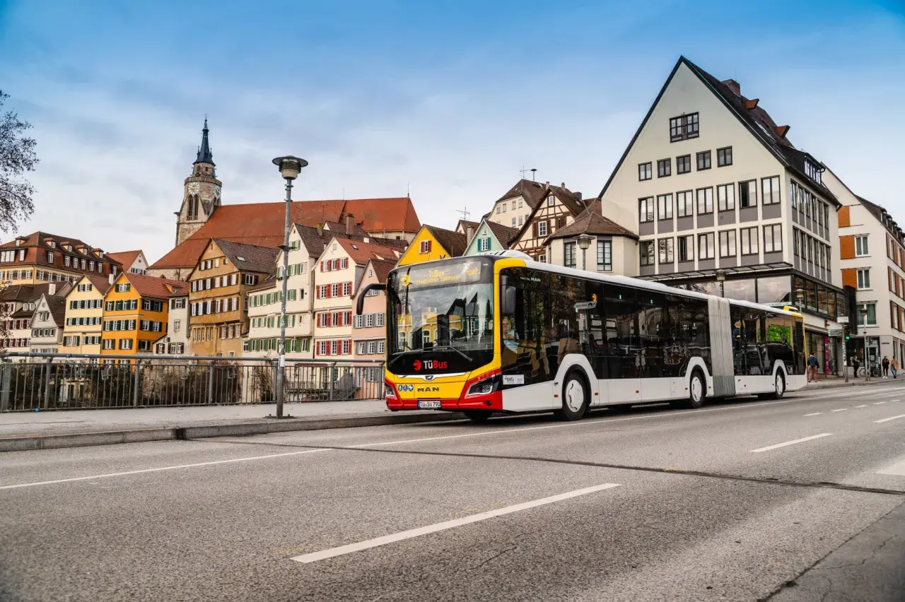 Ein langer ziehharmonika bus fährt an bunten Fachwerkhäusern vorbei.