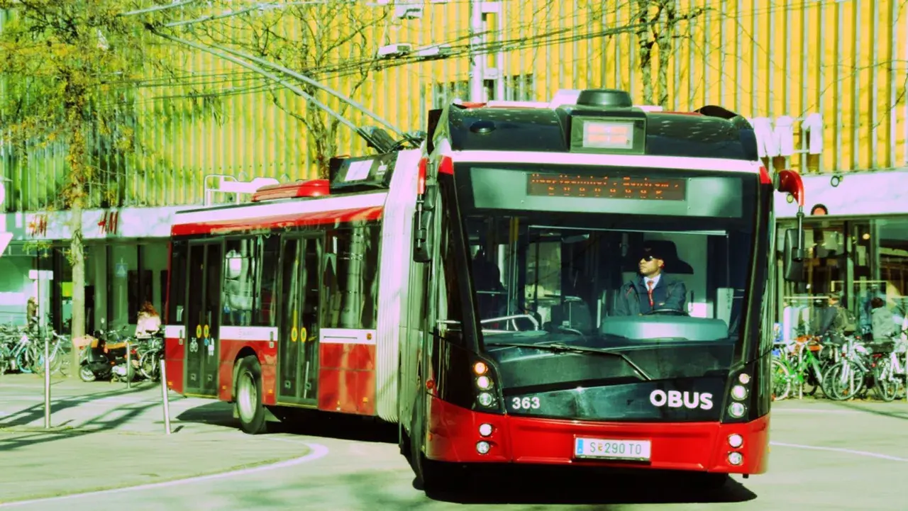 Ein roter Obus mit der Nummer 363 fährt auf der Straße. Der Fahrer trägt eine Sonnenbrille und eine Uniform.