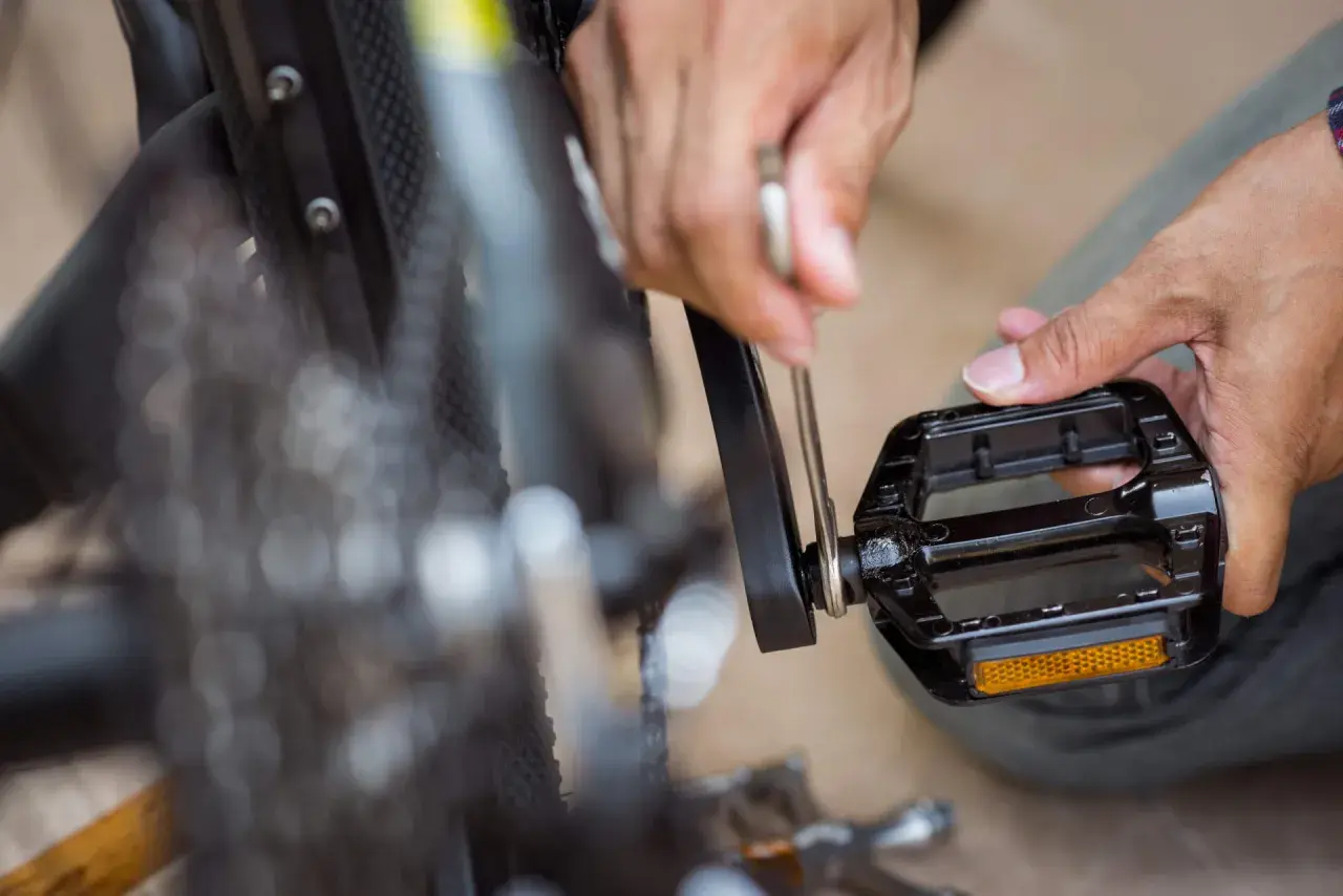 Hände reparieren ein Fahrrad. Ein Werkzeug wird angesetzt, um die Fahrrad Pedale knacken zu beheben.