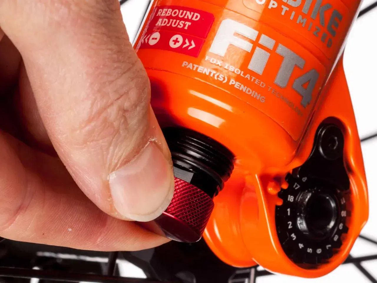 Hand dreht roten Knopf zur Federgabel einstellen. Rebound Adjust ist auf der orangefarbenen Gabel sichtbar.