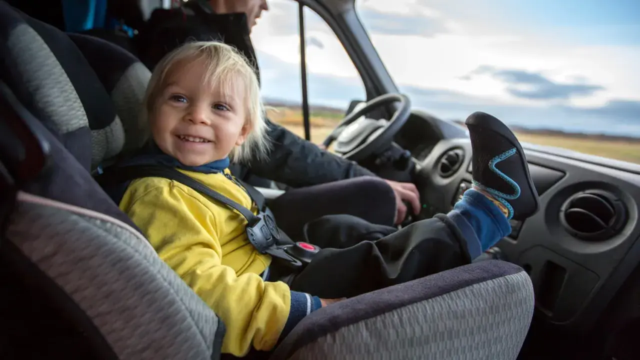 Glückliches Kind im Kindersitz im Bus. Die Füße des Kindes ragen über das Armaturenbrett.