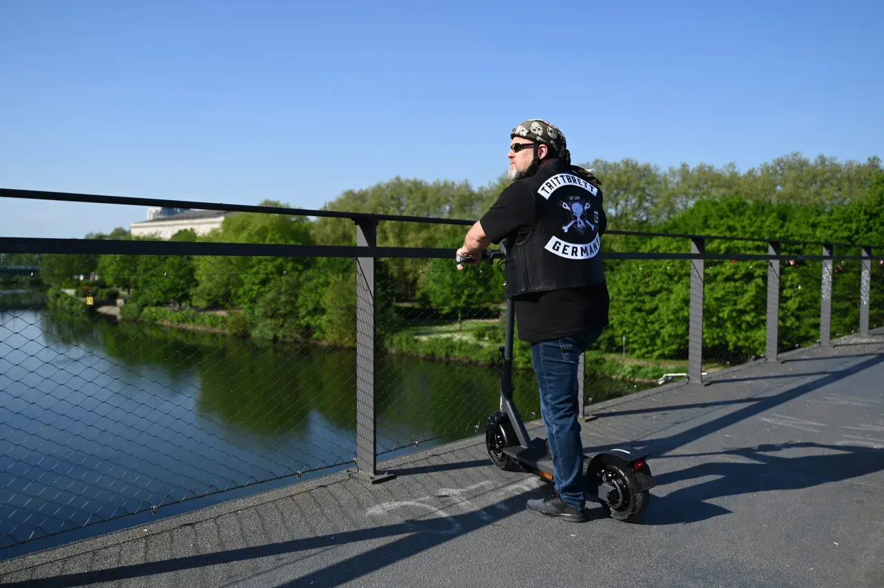 Mann mit Weste und Totenkopf-Bandana auf E-Scooter, genießt die Aussicht. Die Reichweite des E-Scooters ist für die Fahrt über die Brücke ausreichend.
