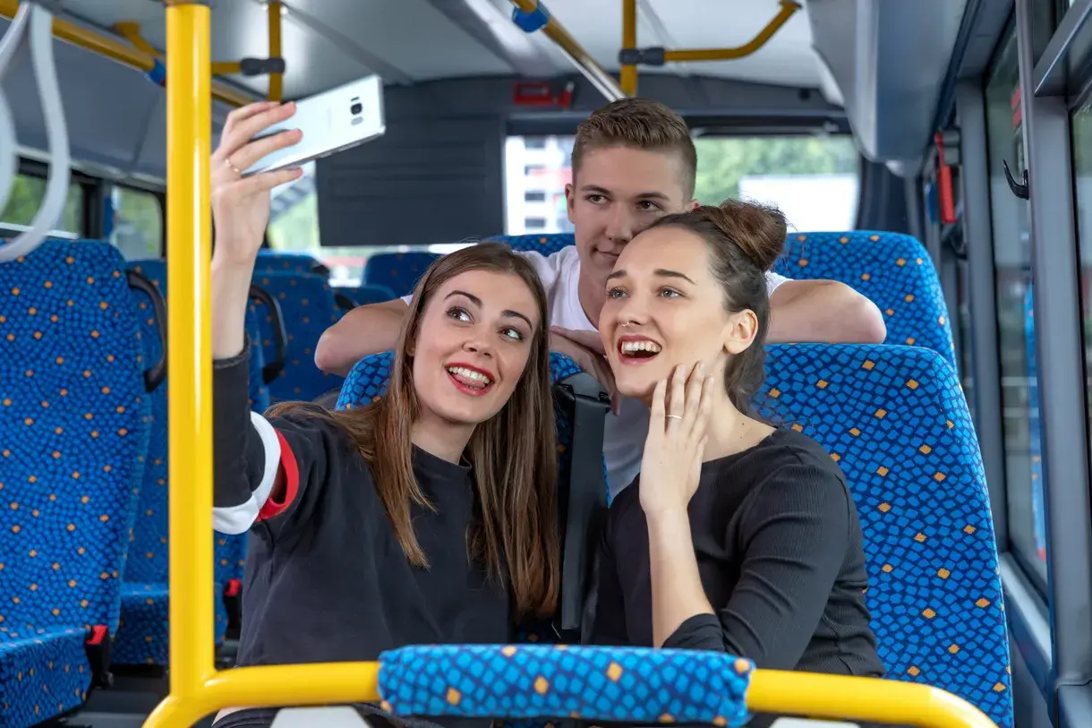 Drei junge Leute machen ein Selfie im Bus. Vielleicht sind sie auf dem Weg zu einem Konzert und hoffen, dass das Transdev Deutschlandticket keine Probleme macht.