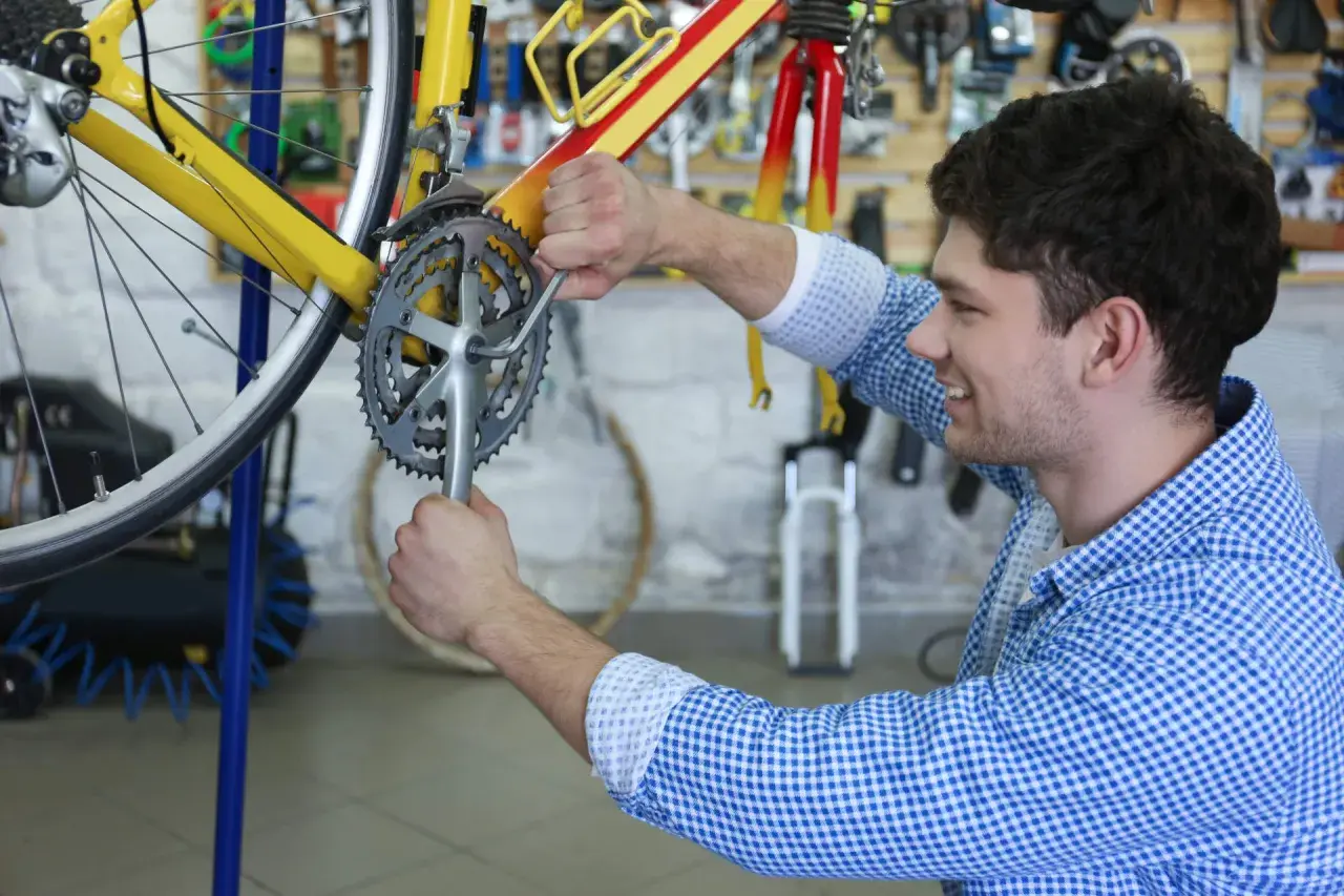 Ein Mann restauriert ein gelbes Fahrrad in einer Werkstatt. Er schraubt mit einem Werkzeug an der Kurbel.