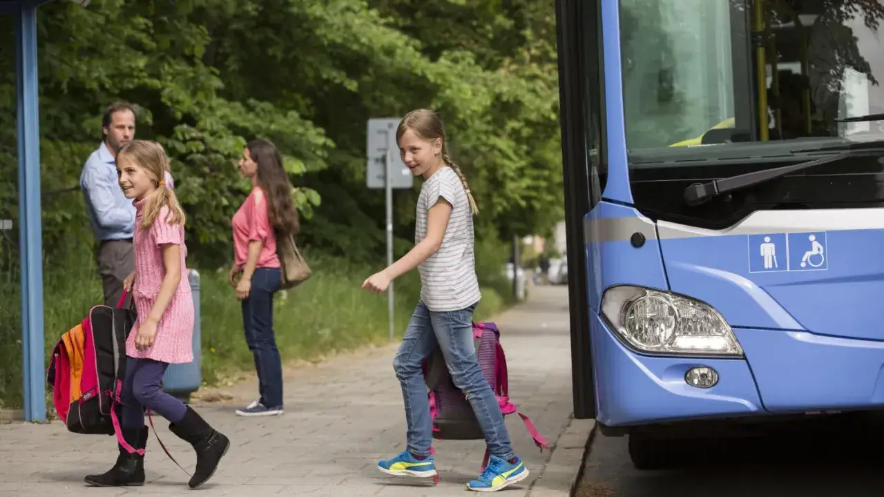 Zwei M&auml;dchen mit Rucks&auml;cken steigen in den blauen Bus.