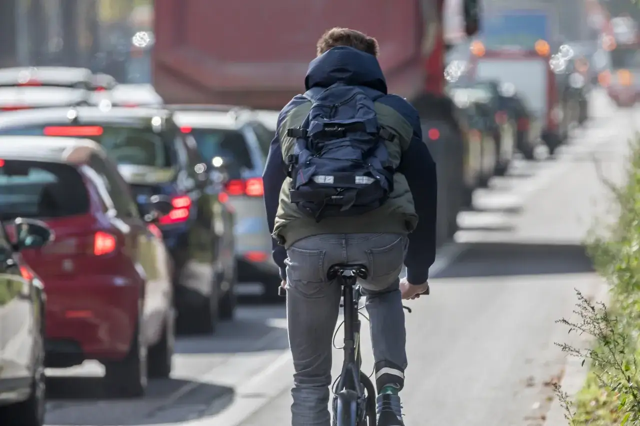 Ein Radfahrer f&auml;hrt im Stau an Autos vorbei. Er hat einen Rucksack auf und tr&auml;gt Jeans. Fahrrad statt Auto ist hier die clevere Wahl.