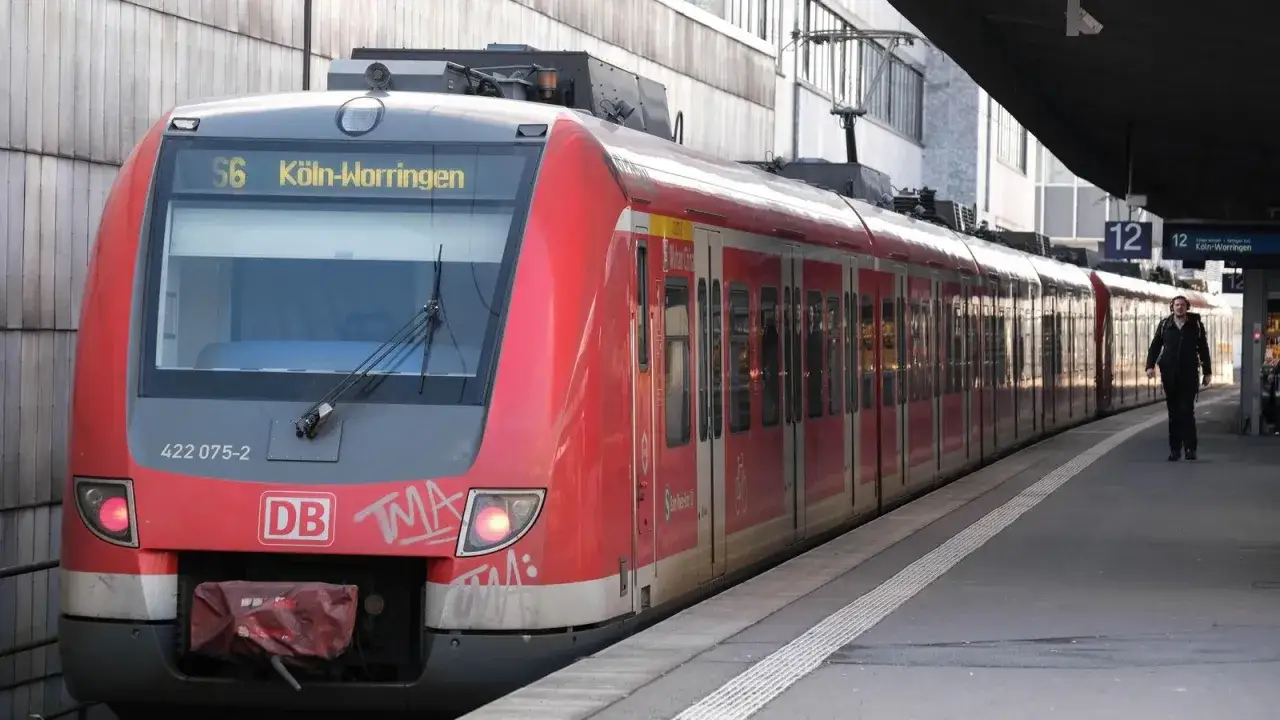 Rote S-Bahn der Linie S6 K&ouml;ln-Worringen steht am Bahnsteig. Ein Mann mit Rucksack geht entlang des Zuges.