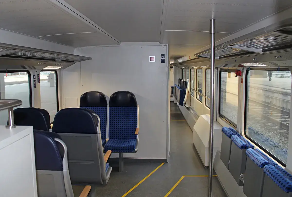 Innenraum eines Bombardier Doppelstockwagens mit blauen Sitzen und Blick auf den Bahnsteig.