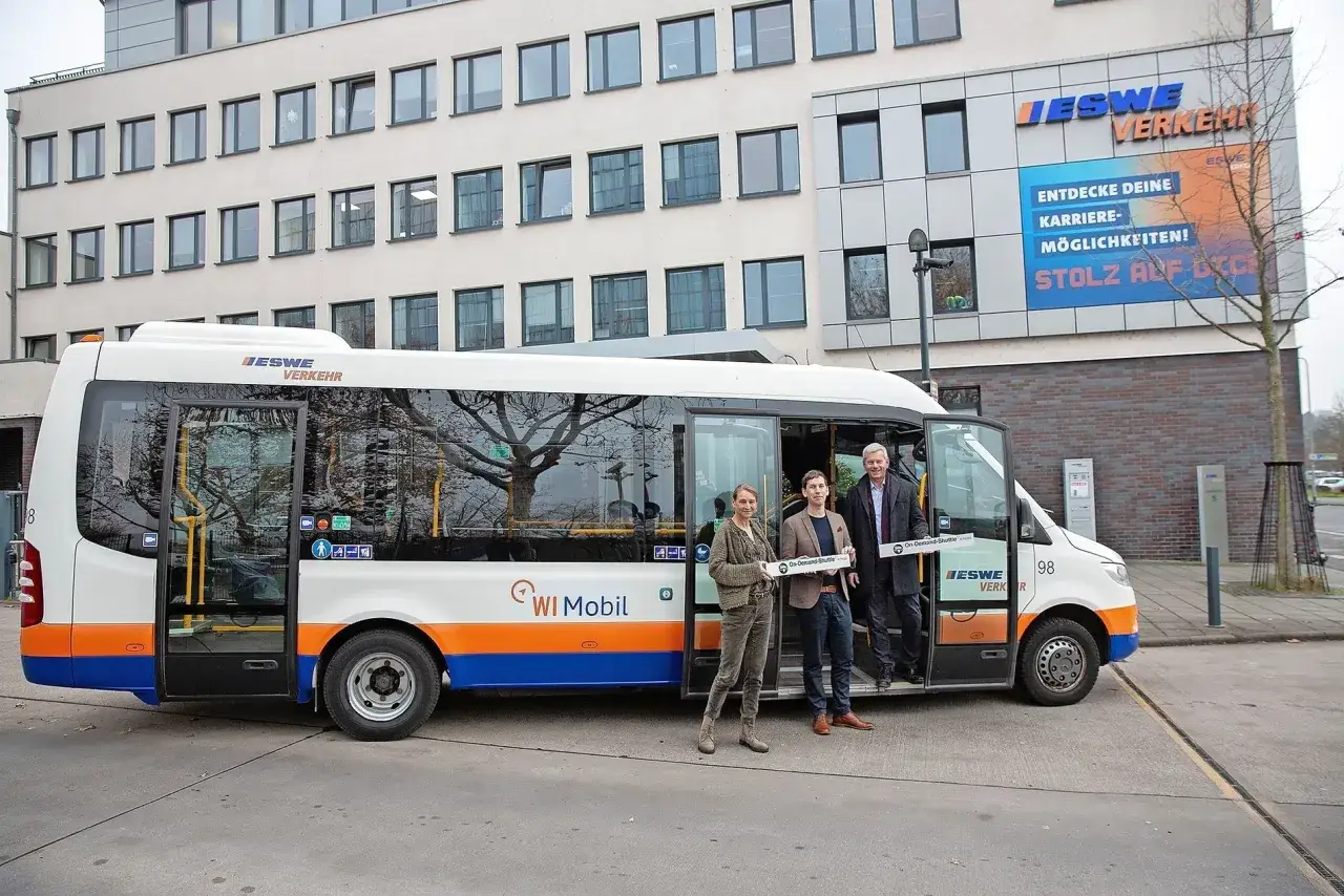 Drei Personen stehen vor einem Kleinbus mit der Aufschrift 