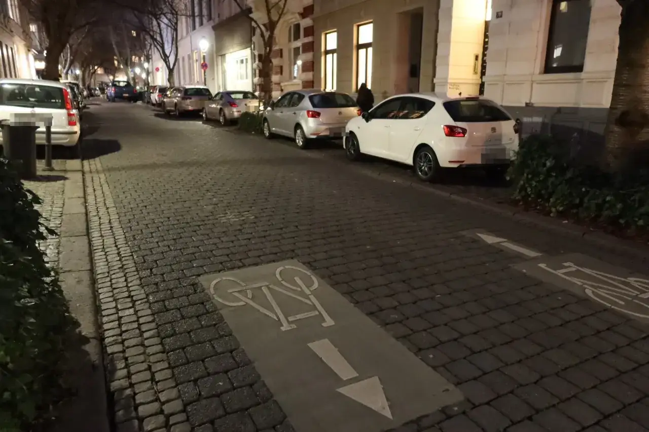 Radweg mit Fahrradsymbol auf Kopfsteinpflaster. Ein wei&szlig;es Auto parkt am Stra&szlig;enrand.