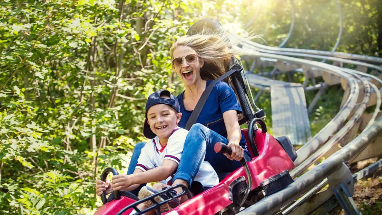 Ein Junge und seine Mutter haben Spa&szlig; auf einer Rodelbahn in NRW. Die Sonne scheint, die Haare wehen im Wind.