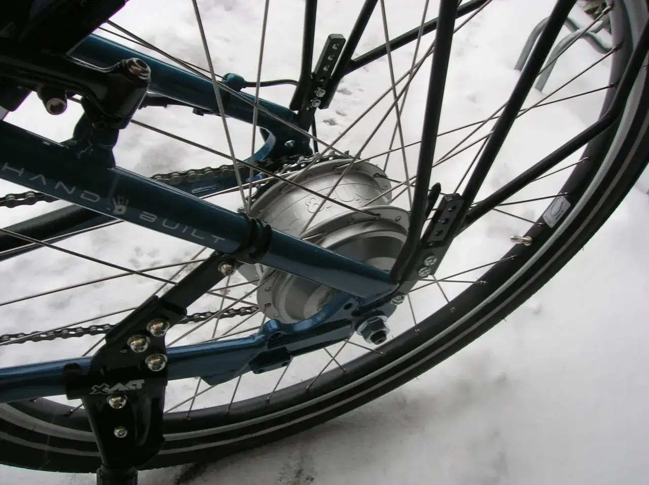 Das Hinterrad eines Fahrrads mit einem Bafang Motor im silbernen Gehäuse, das im Schnee steht.