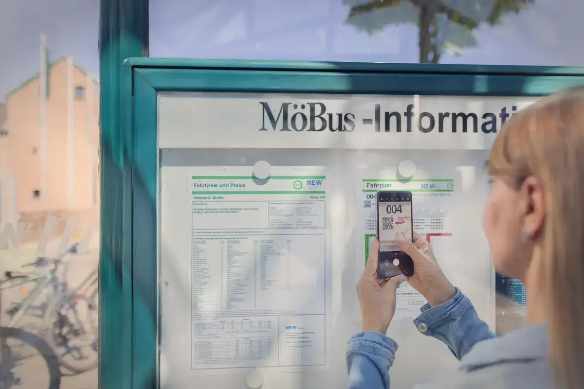 Frau scannt QR-Code am Busfahrplan. So findet man auch an Feiertagen in NRW schnell die richtigen Busse.