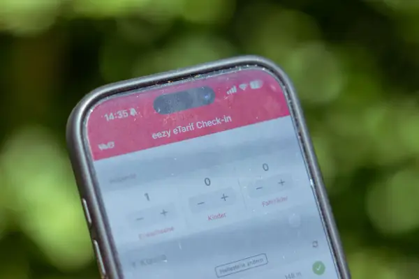 Ein Smartphone zeigt die "eezy eTarif Check-in" App. Ein Erwachsener und ein Kind sind für die Fahrt ausgewählt.