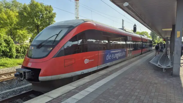Roter Zug der euregiobahn br 643 steht am Bahnsteig. Grüne Bäume und blauer Himmel im Hintergrund.