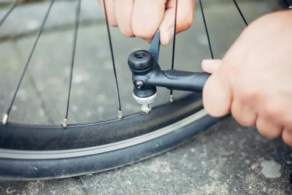 Hände pumpen mit einer Handpumpe Luft in ein Fahrradventil.